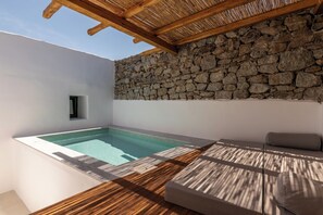 A modern outdoor pool area with a stone wall, wooden deck, and a built-in seating area. - Mykonos Drops (Mykonos)