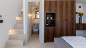 A modern bedroom with a large bed, a wooden wardrobe, and a bathroom visible through an open door. - Mykonos Drops (Mykonos)