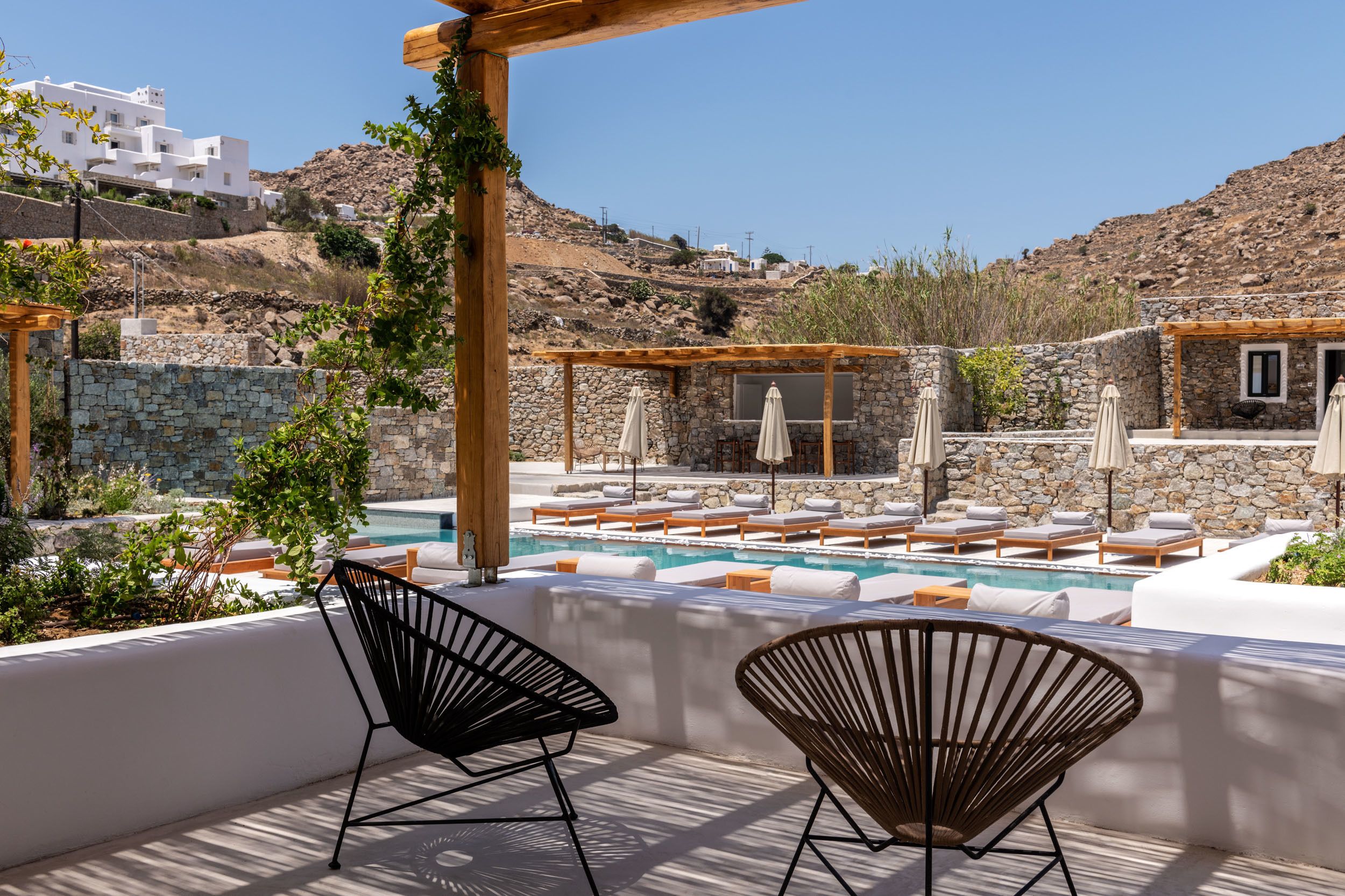 A poolside area with stone walls, lounge chairs, and umbrellas.
