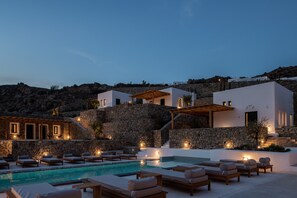 A poolside area with lounge chairs and a stone wall. - Mykonos Drops (Mykonos)