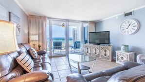Una sala de estar con un sofá de cuero, una mesa de centro de vidrio, un televisor y un balcón con vistas.
