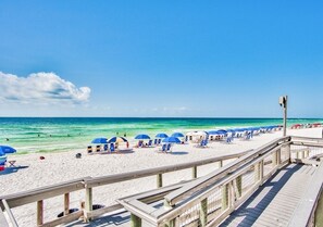 A beach with a wooden boardwalk, blue umbrellas, and beach chairs.