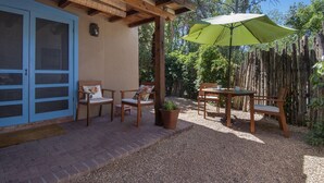 Un patio con sillas y mesa de madera, una sombrilla verde y una valla de madera.