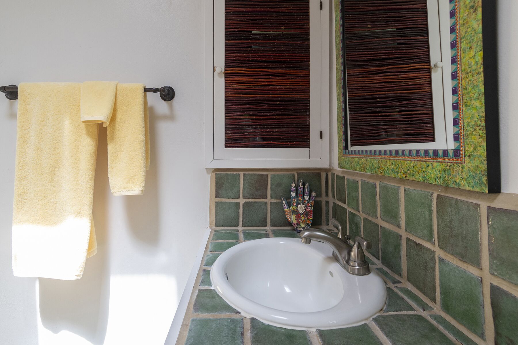 A bathroom with a white sink, green tiled backsplash, and a window with brown shutters.