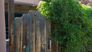 Una verja de madera con un pestillo metálico, parcialmente cubierta por follaje verde.