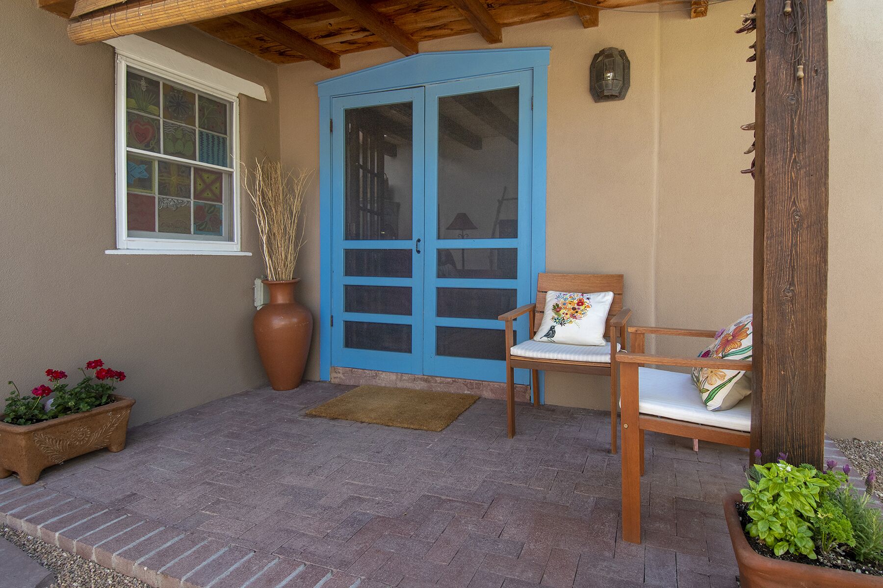 A covered porch with a blue door, a wooden bench with a cushion, and potted plants.