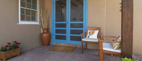 A covered porch with a blue door, a wooden bench with a cushion, and potted plants.