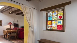 Una habitación con un banco de madera, un sofá rojo, una mesa de comedor con sillas y un ventanal con vidrieras de colores.