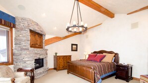A bedroom with a stone fireplace, a large bed, a chair, and a nightstand. - Spacious 4500Sq/Ft - 5 Bed 5.5 Bath - Theater - Ski, Shop, Dine Within Steps! (Park City)