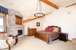 A bedroom with a stone fireplace, a large bed, a chair, and a nightstand.