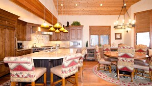 A spacious kitchen with wooden cabinets, a large island with bar stools, and a dining area with a round table and chairs. - Spacious 4500Sq/Ft - 5 Bed 5.5 Bath - Theater - Ski, Shop, Dine Within Steps! (Park City)