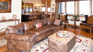 A spacious living room with a large brown leather sofa, a patterned ottoman, and a mounted deer head on the wall. - Spacious 4500Sq/Ft - 5 Bed 5.5 Bath - Theater - Ski, Shop, Dine Within Steps! (Park City)