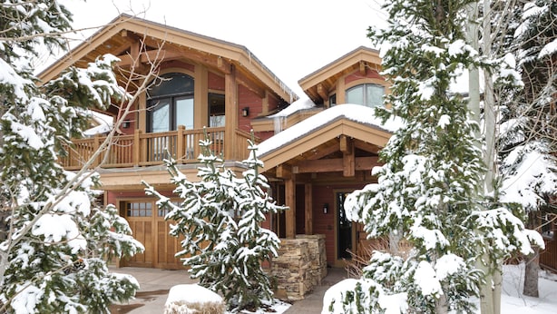 A two-story log cabin with a balcony, stone foundation, and snow-covered surroundings. - Spacious 4500Sq/Ft - 5 Bed 5.5 Bath - Theater - Ski, Shop, Dine Within Steps! (Park City)