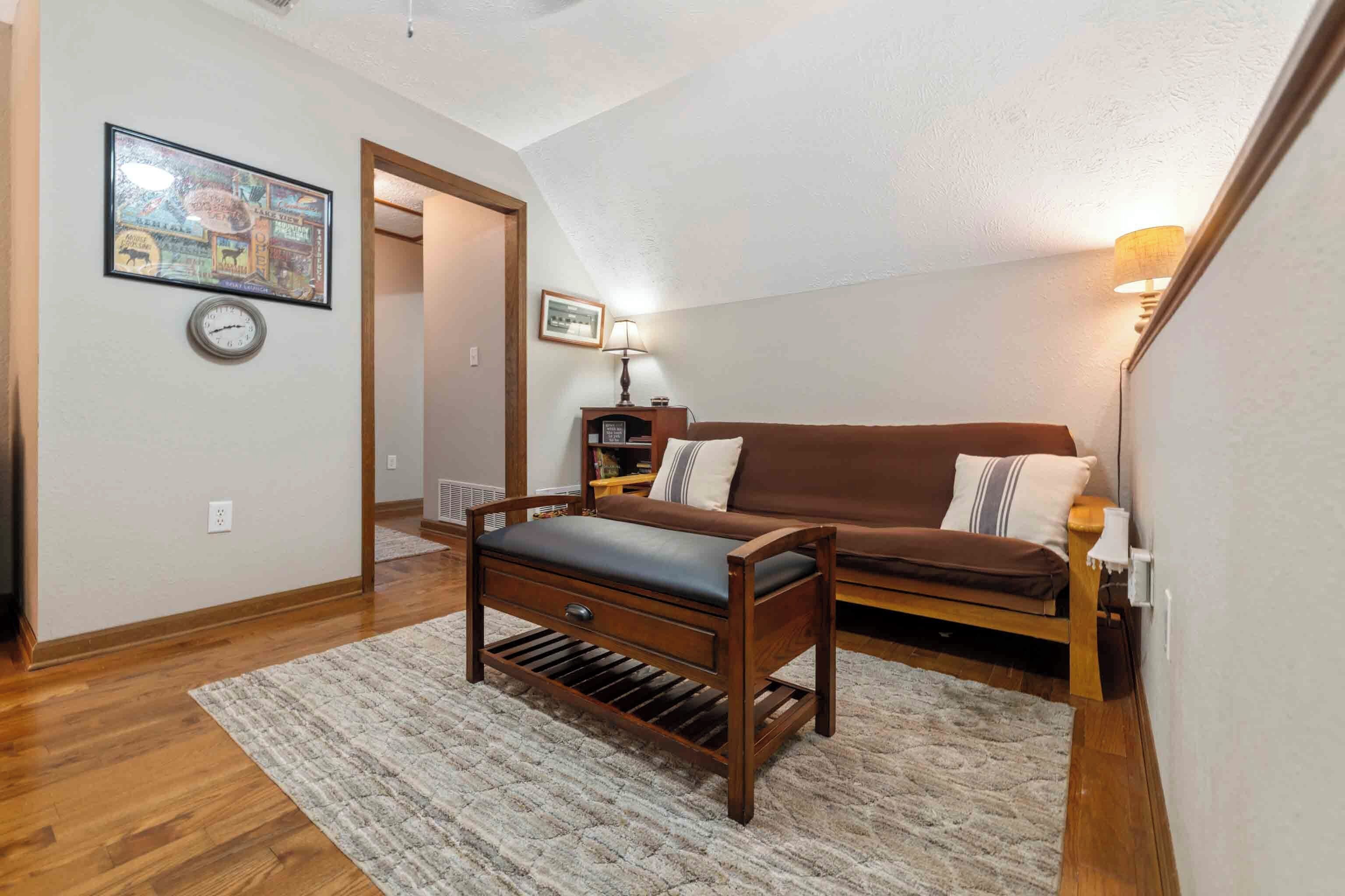 A cozy room with a wooden bench, a brown sofa, a rug, and a wall clock.