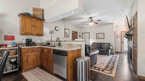 A spacious kitchen with wooden cabinets, a dishwasher, and a granite countertop. There is a dining area with a leather couch and a rug. - Your Home Base for the Little Red River, Trout Fishing & Greers Ferry Lake (Heber Springs)