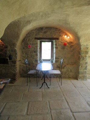 A stone-walled room with a round table and four chairs, a small window, and a stone floor.