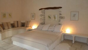 Ein Schlafzimmer mit einem großen Bett, zwei Nachttischen, einer Steinwand und gerahmten Kunstwerken.