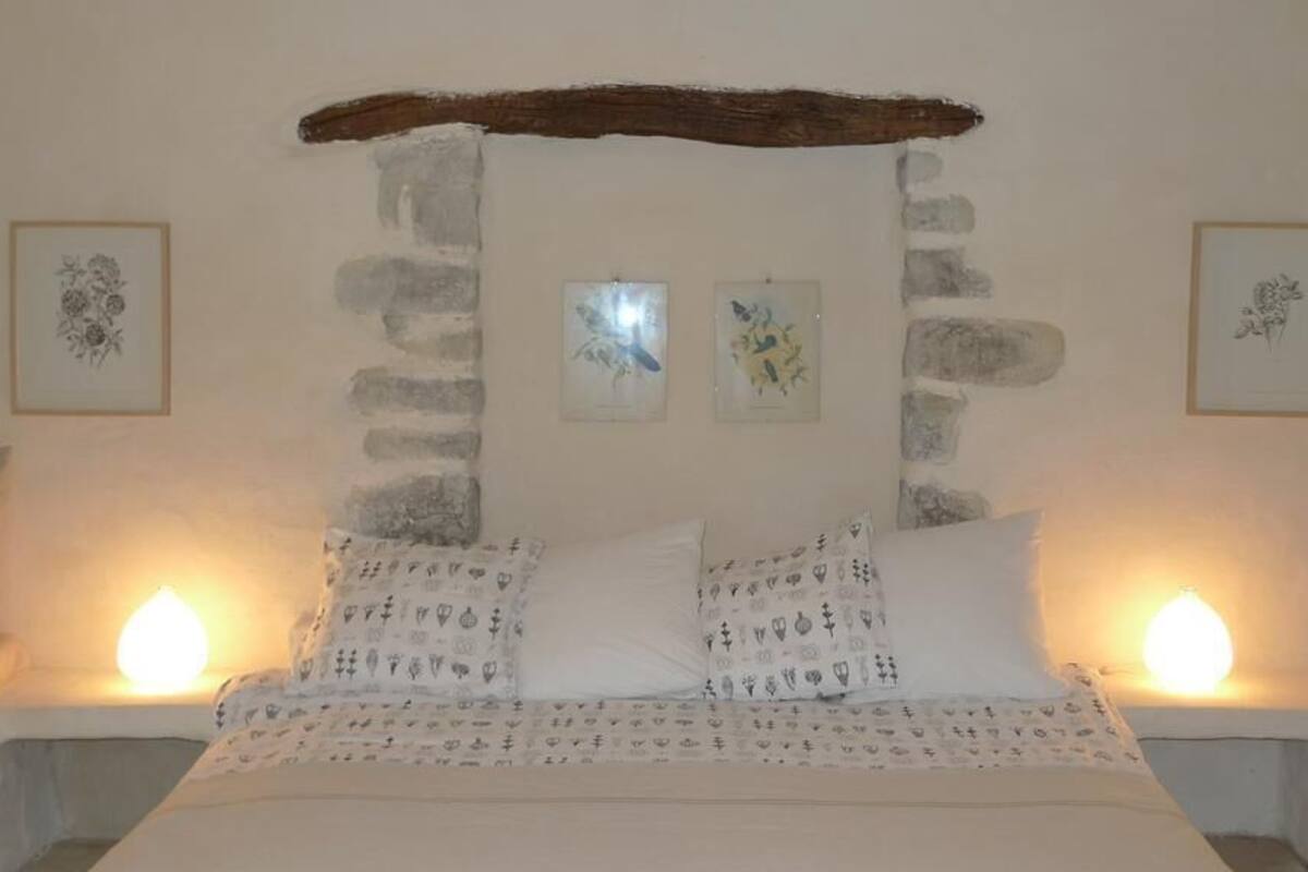 Ein Bett mit gemusterten Betttextilien, eine Steinwand und gerahmte Kunstwerke an den Wänden.
