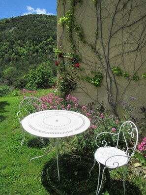 A white metal table and chair set in a garden with pink flowers and greenery.