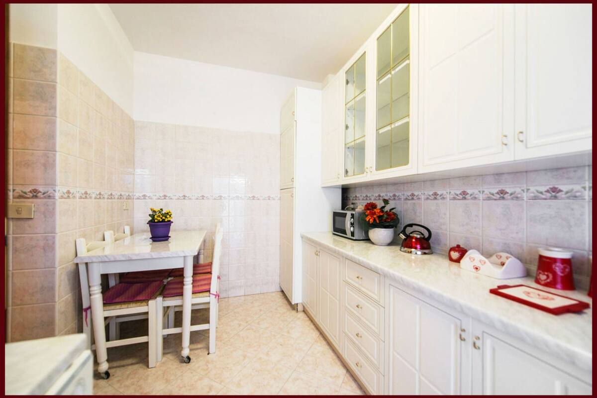A kitchen with white cabinets, a marble countertop, and a dining table with chairs.