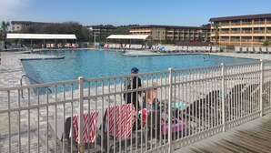 Une piscine entourée d’une clôture blanche, avec des chaises longues et un bâtiment en arrière-plan.
