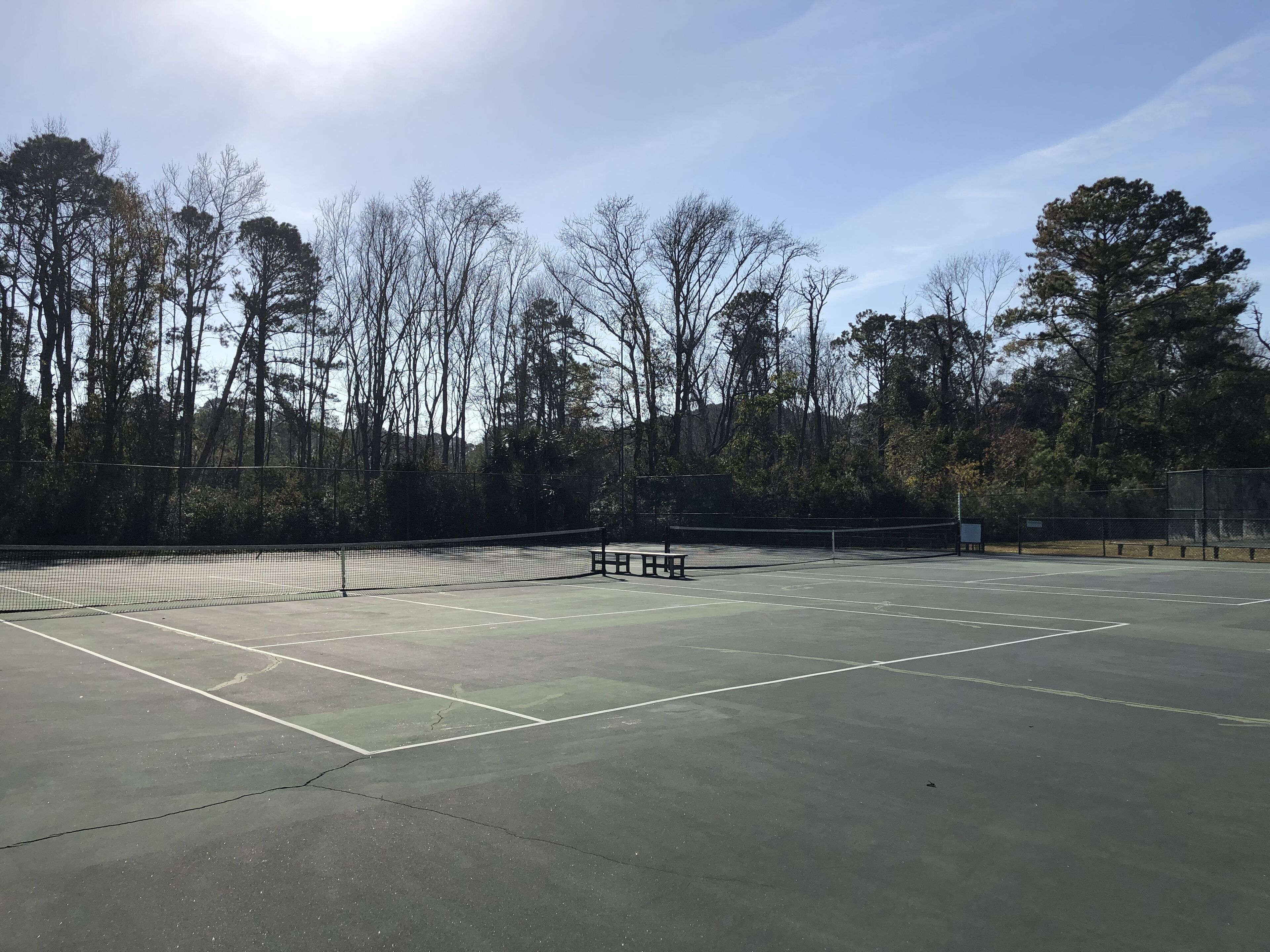 An outdoor tennis court with a net, benches, and trees in the background.