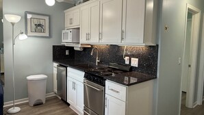 Une cuisine moderne avec des meubles blancs, un plan de travail noir, une cuisinière en acier inoxydable et un ventilateur de plafond.