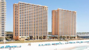 Un hôtel situé en bord de mer, composé de plusieurs immeubles de grande hauteur, doté d’une plage de sable et de nombreux parasols.