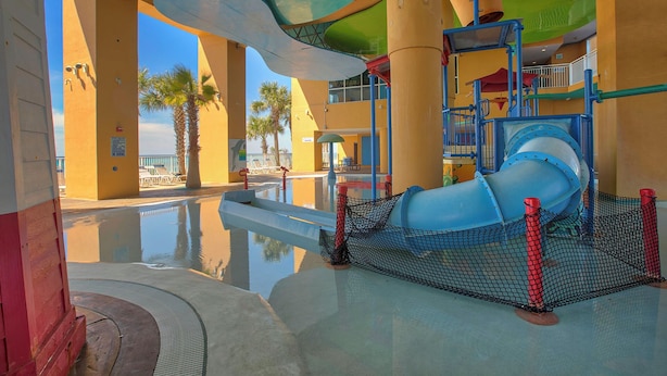 Un parc aquatique avec un toboggan bleu, des palmiers et un espace piscine.