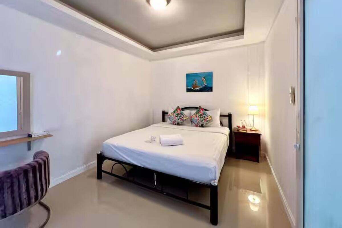 Een slaapkamer met een bed, nachtkastje, lamp, raam en een schilderij aan de muur.