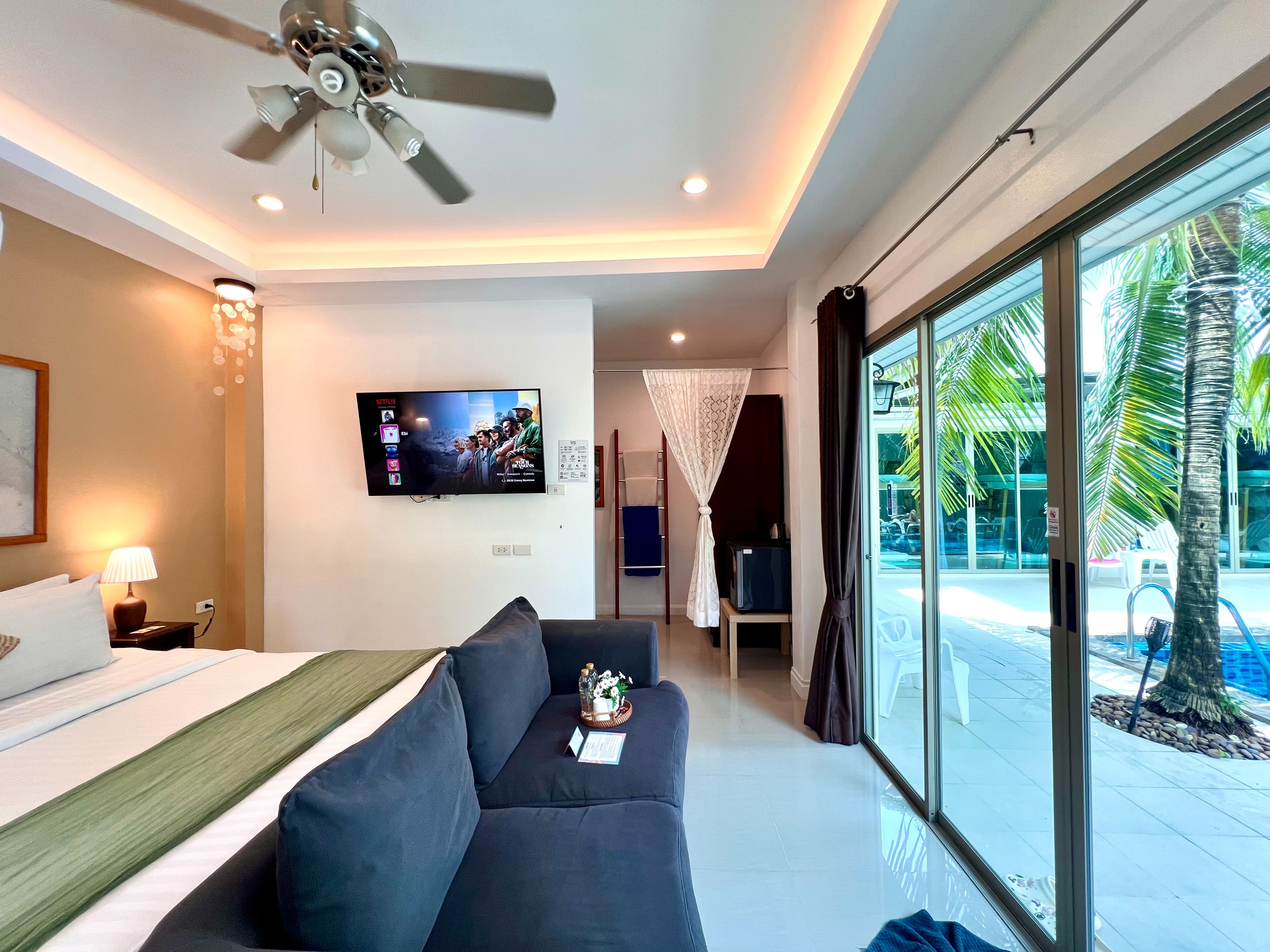 Habitación de hotel con cama, sofá, televisión, ventilador de techo y vistas al exterior.