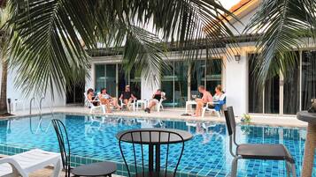 Uma área à beira da piscina com azulejos, espreguiçadeiras e palmeiras.