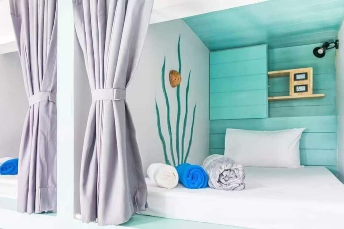 Een kamer met een bed, nachtkastje, wandplank en gordijn.