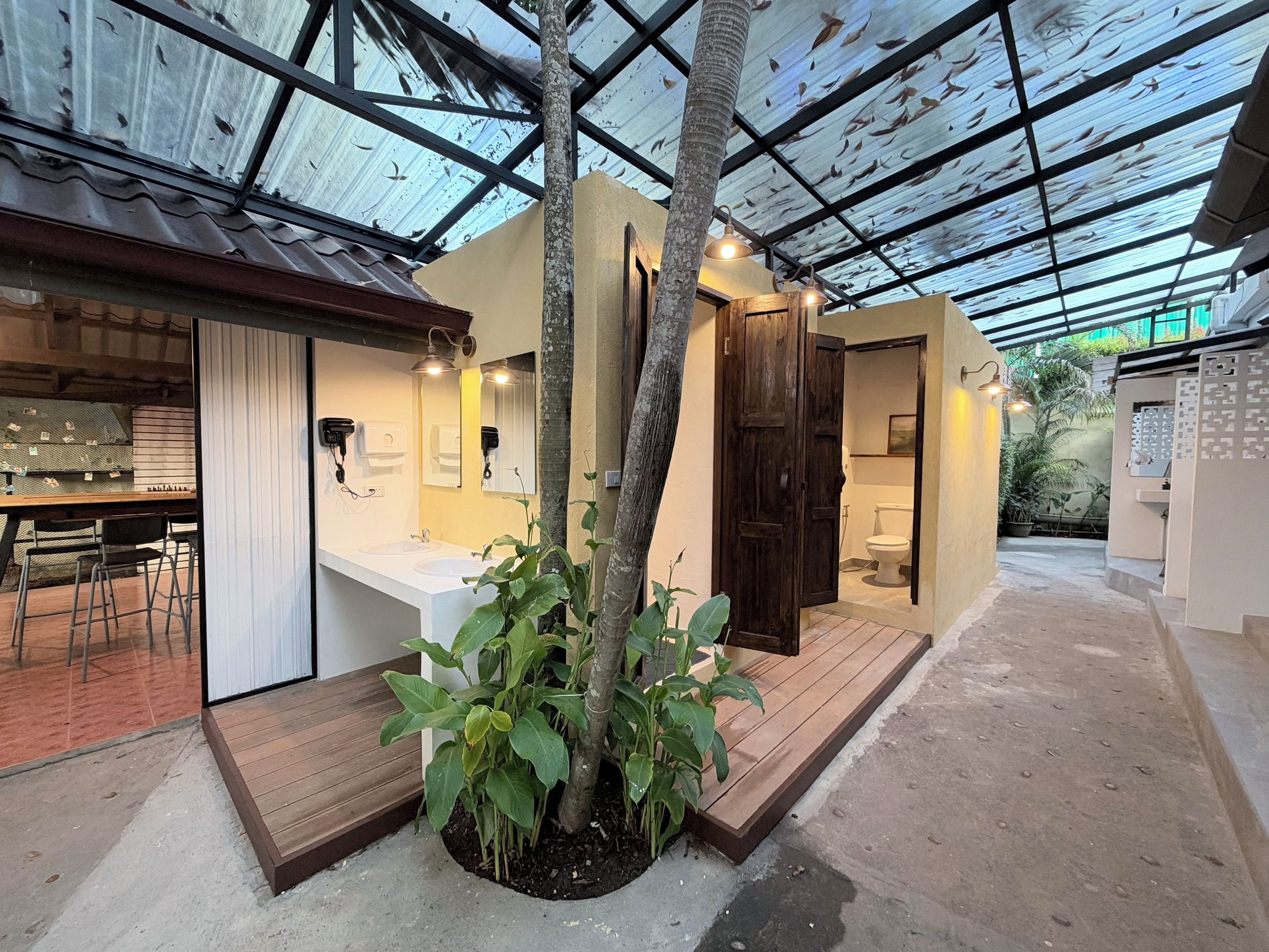 A compact, modern bathroom with a wooden door, a sink, and a toilet. There is a small plant in the center.