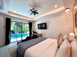 Un dormitorio con cama, televisor, ventilador de techo y vista a una piscina exterior.