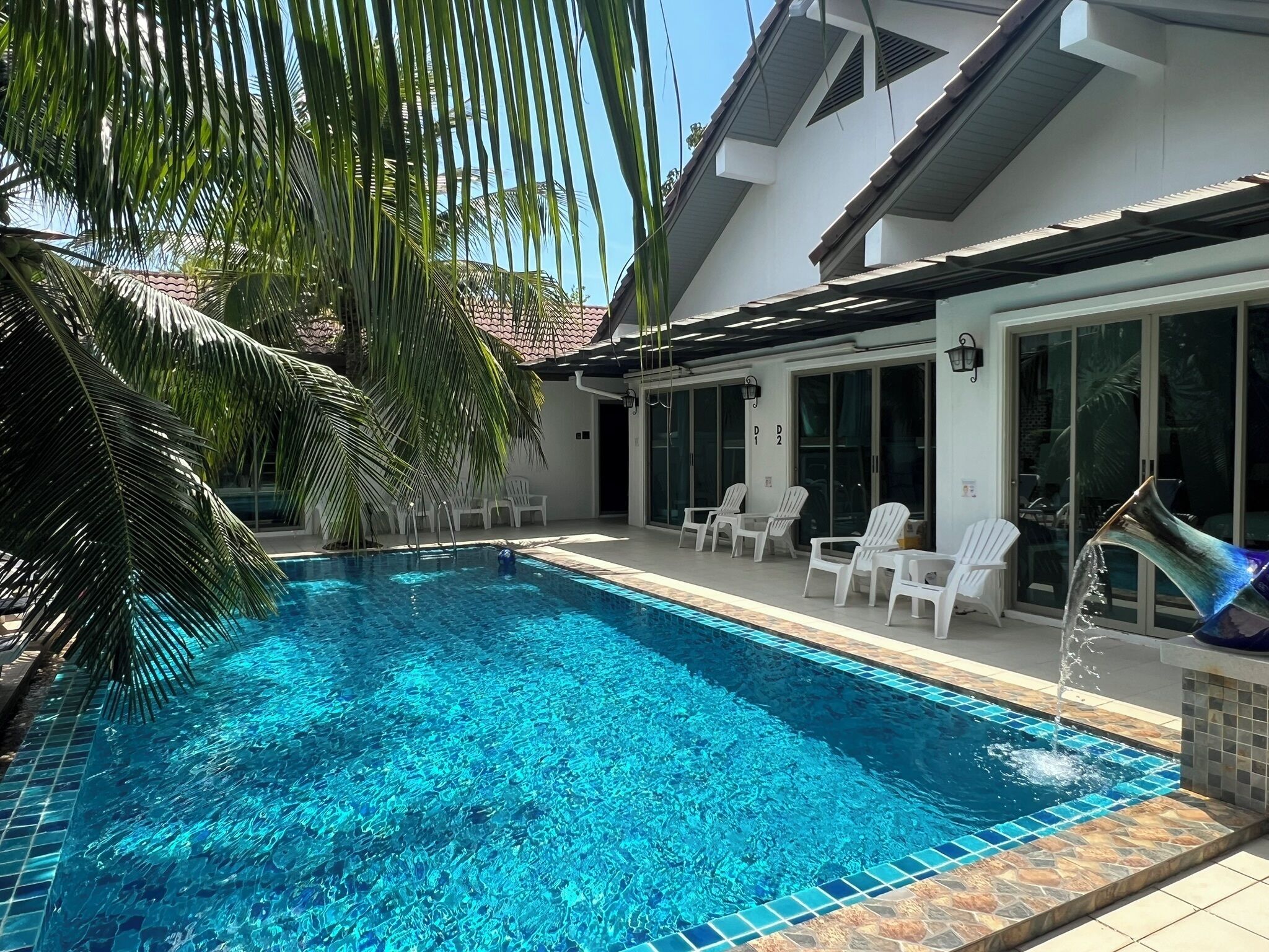 Una piscina con agua cristalina azul, rodeada de sillas blancas y palmeras.