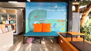 Een kamer met een muurschildering van een walvis en een vliegtuig, een bed met oranje kussens, een kleine tafel en een rugzak op de vloer.