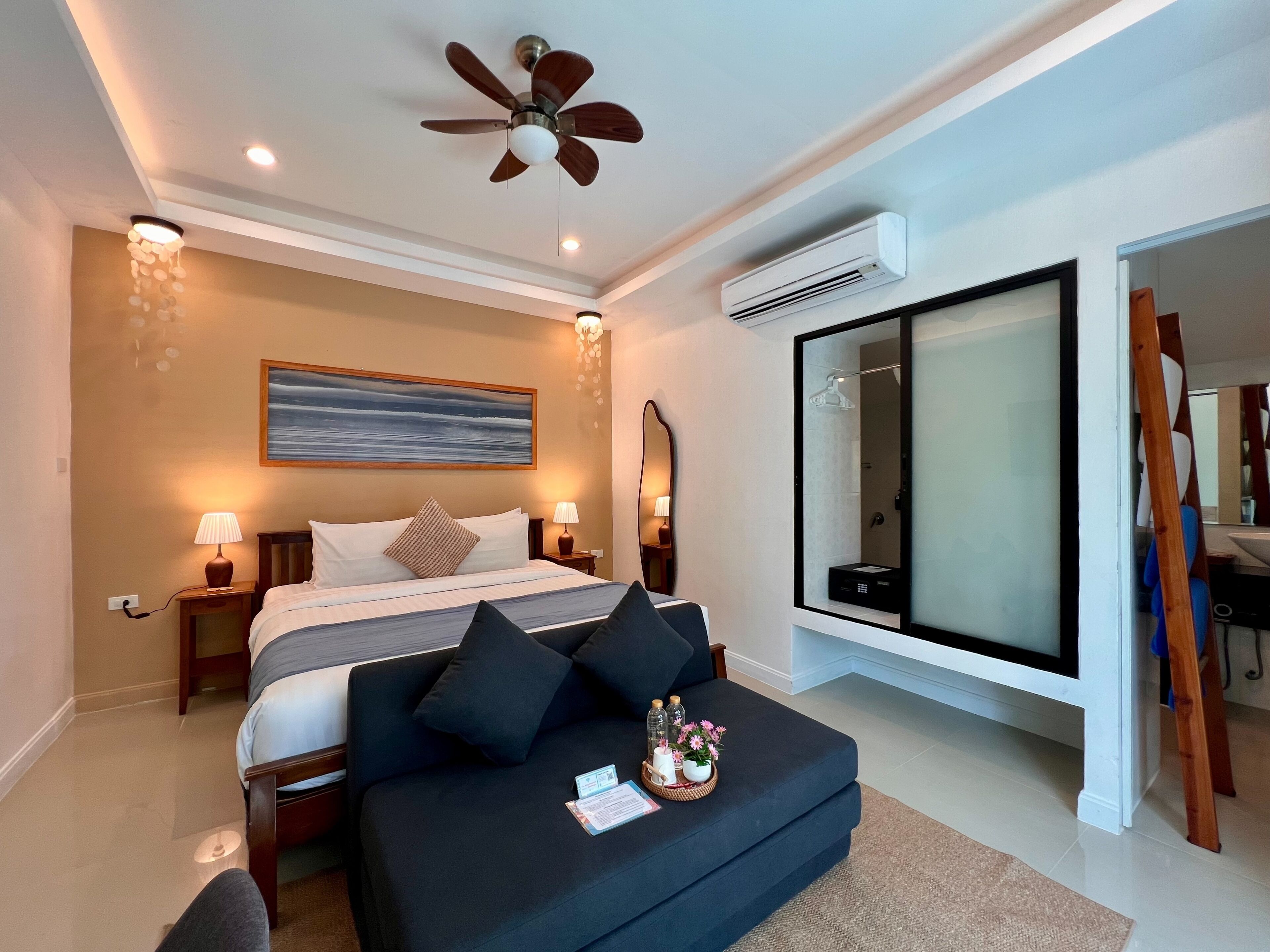 Une chambre d’hôtel moderne équipée d’un lit, de lampes de chevet, d’un ventilateur de plafond, d’un climatiseur, d’un grand miroir et offrant une vue sur l’extérieur.