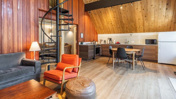 A modern interior with a spiral staircase, wooden walls, a kitchen, and a seating area with a sofa and chairs.