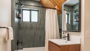 A modern bathroom with a bathtub, a shower, a vanity with a mirror, and a window.