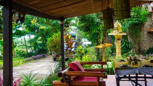 Un espace extérieur abrité, aménagé avec un banc et une table, entouré d’une végétation luxuriante et bordé d’un sentier.