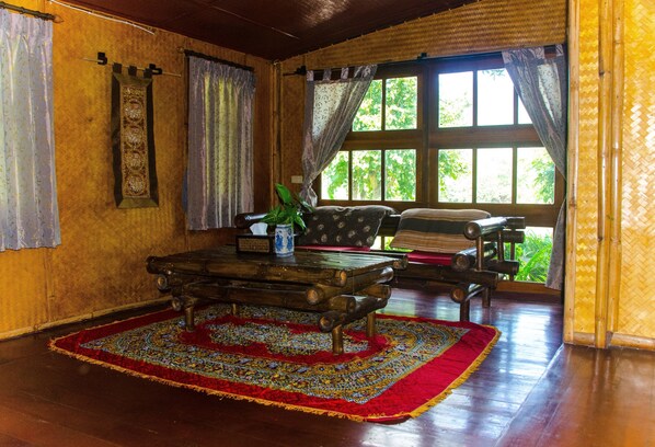 A room with a wooden floor, a patterned rug, a bench, and a window with curtains. - Yoga Art Home (Mae Ai)