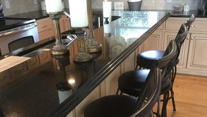 A kitchen with a black countertop, wooden cabinets, and a bar area with black stools. - #1 Rated Vacation Home w/ Deep Water on the Main Channel (Taylorsville)