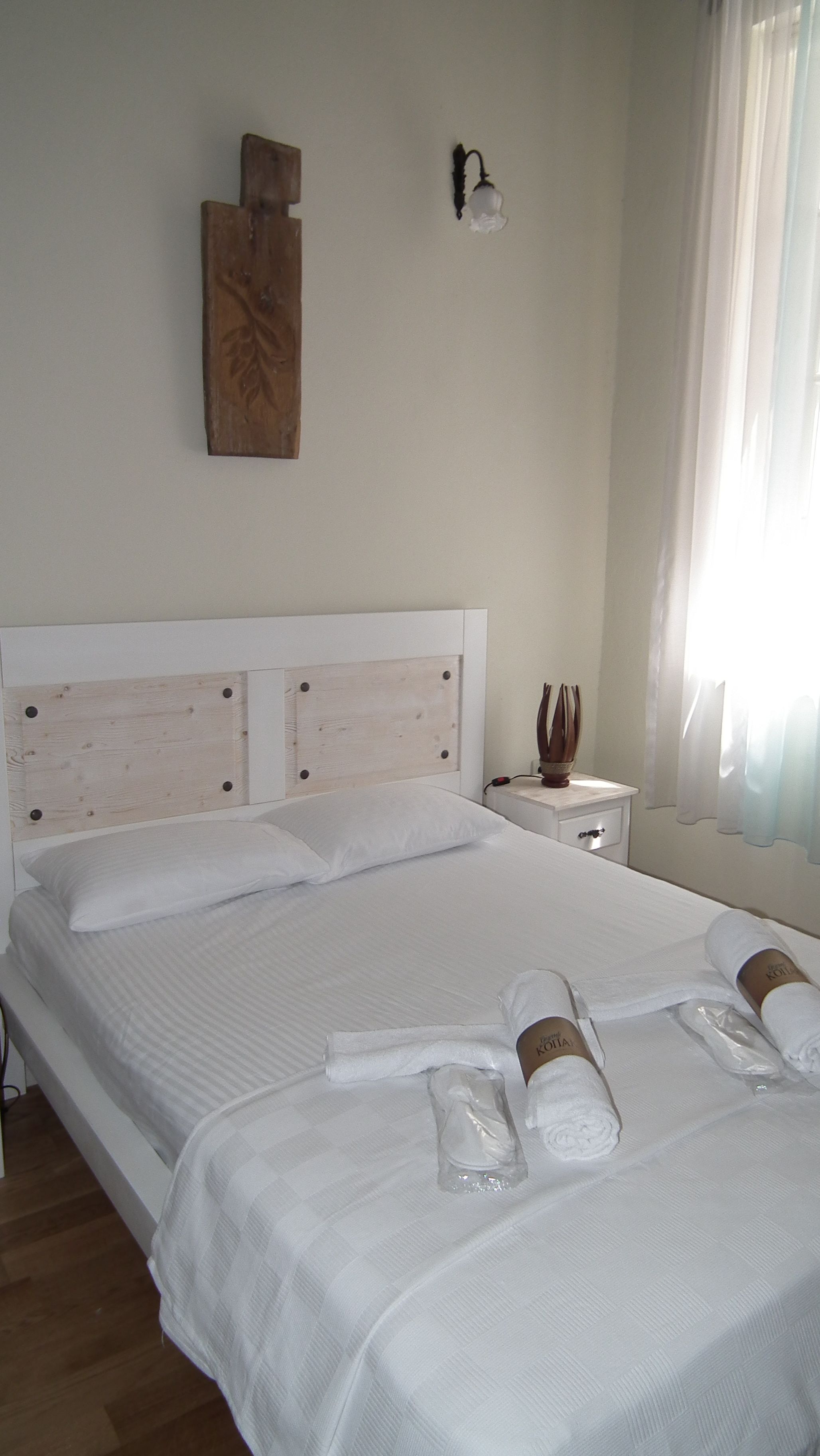 Un lit bien fait, avec du linge de lit et des serviettes blanches, une tête de lit en bois, une table de chevet avec une lampe et un luminaire fixé au mur.