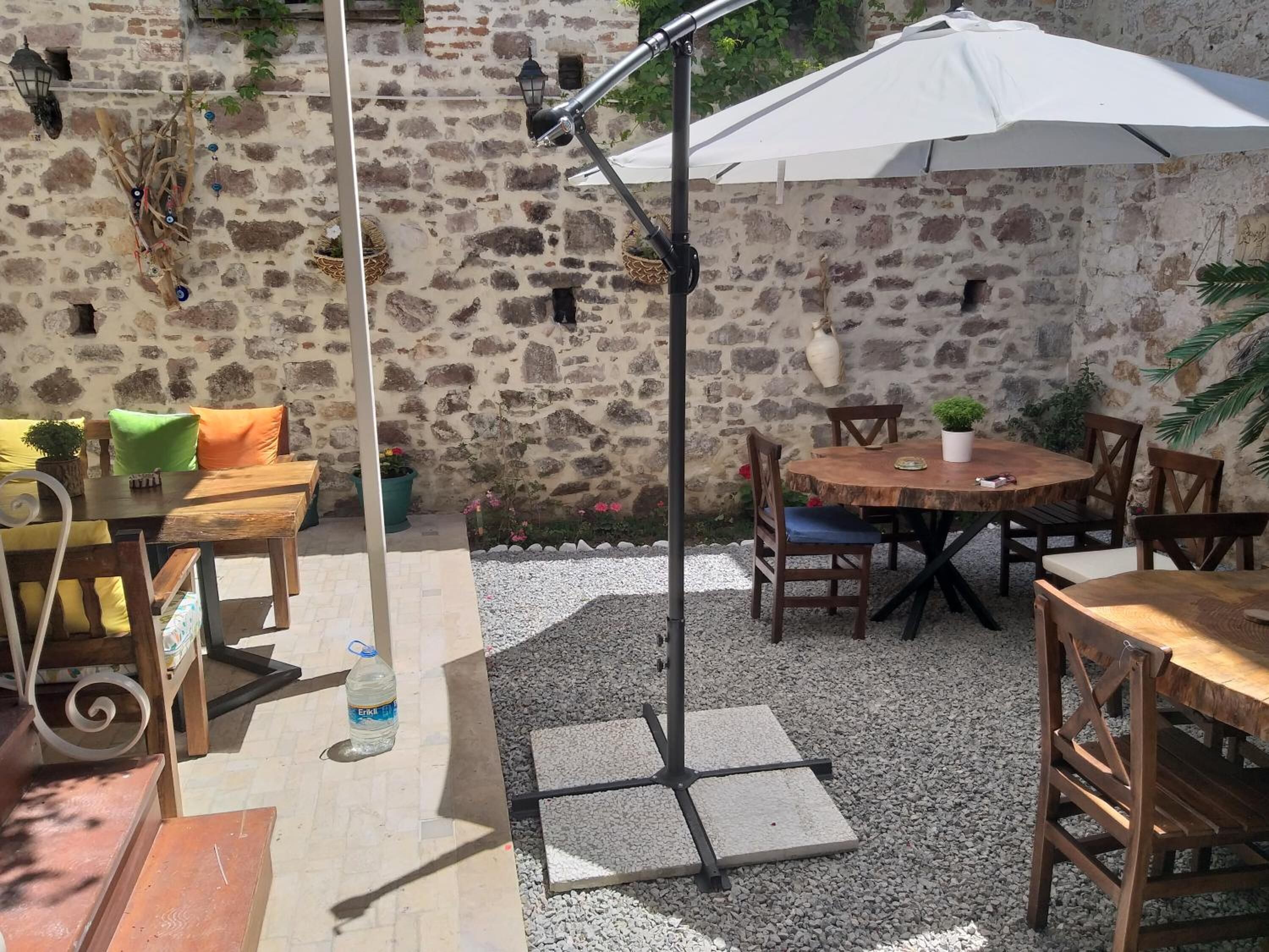 A stone-walled outdoor patio with wooden furniture, a white umbrella, and a water bottle on the table.