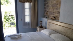 A neatly made bed with white linens and towels, a wooden nightstand with a lamp, and a stone wall. - Gizemli Konak (Ayvalik)