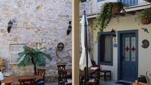 An outdoor seating area with stone walls, wooden tables and chairs, a potted plant, and hanging baskets. - Gizemli Konak (Ayvalik)