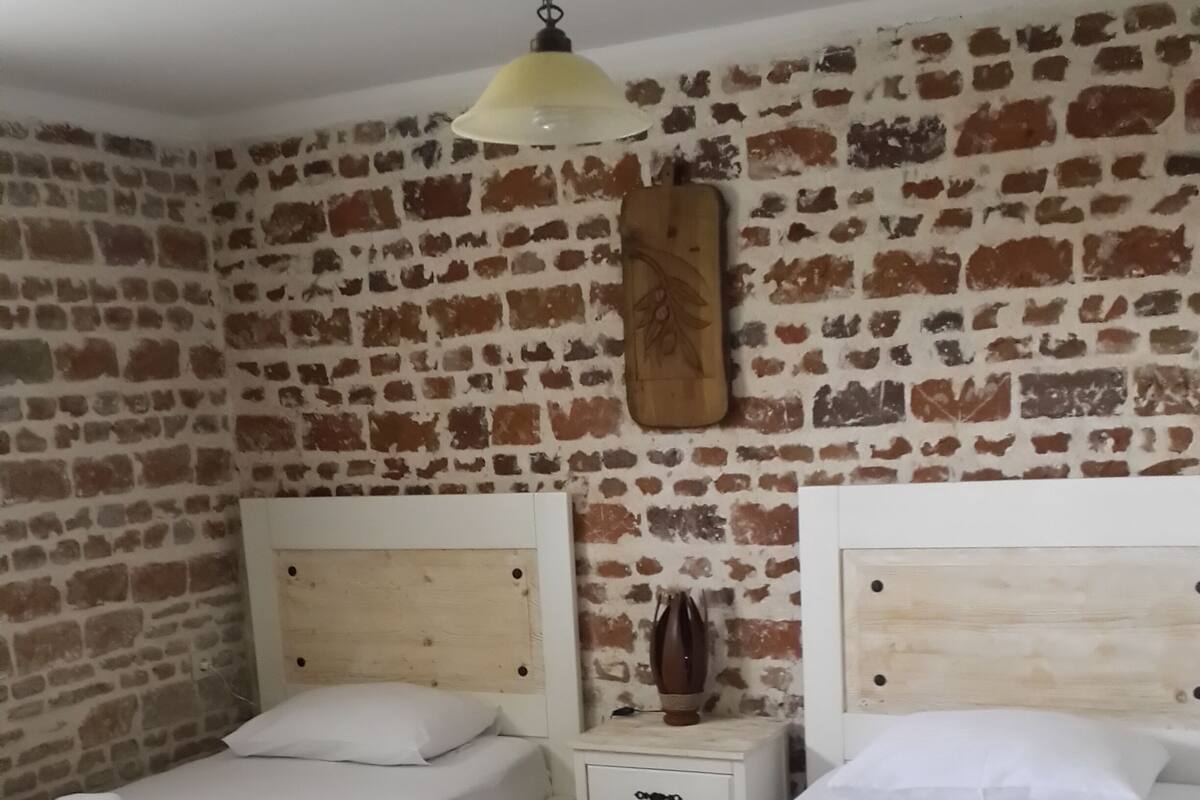 A room with two beds, a brick wall, a wooden headboard, a nightstand, and a hanging lamp.
