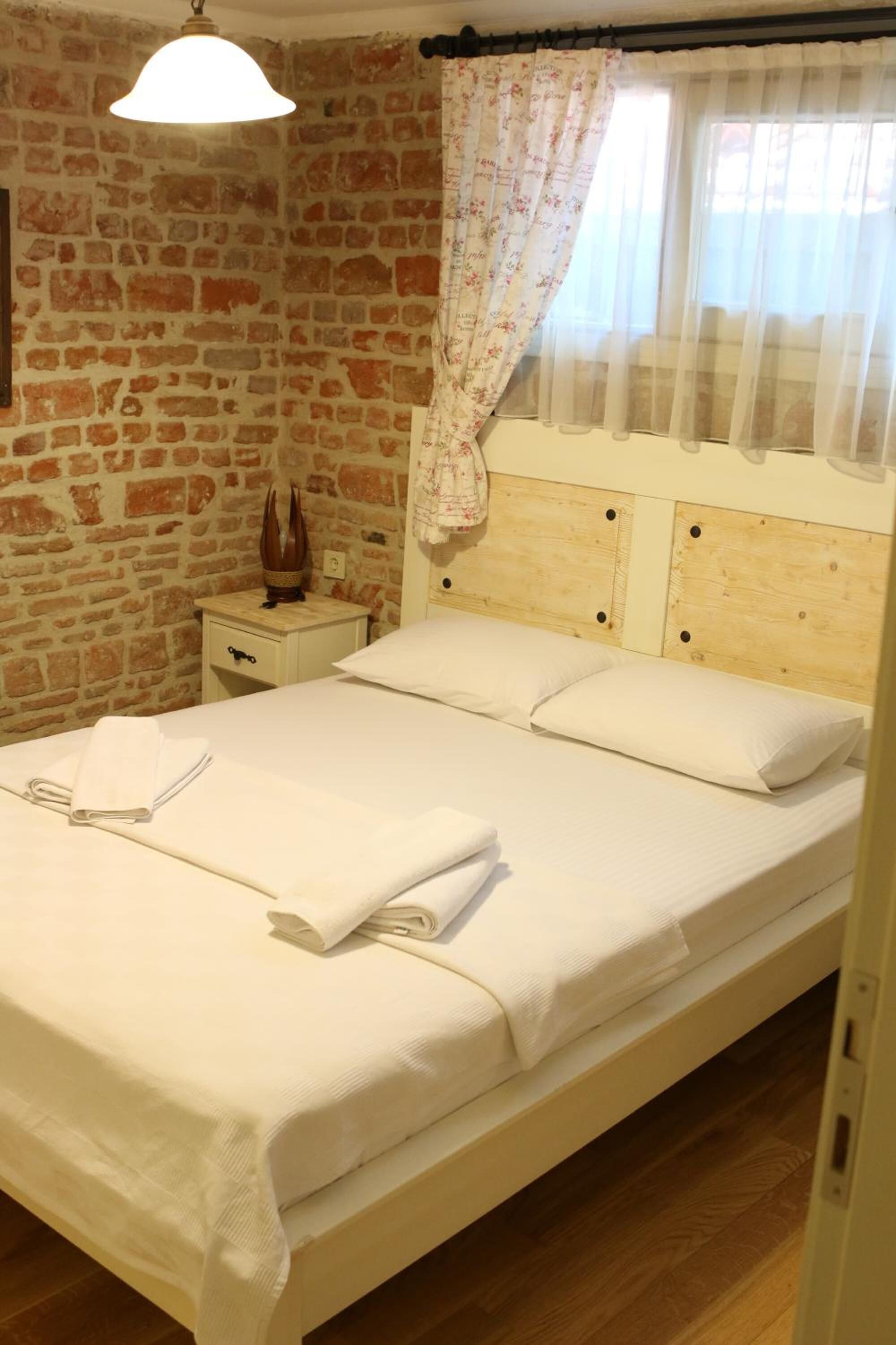 A bed with white linens, a nightstand with a decorative item, and a brick wall.