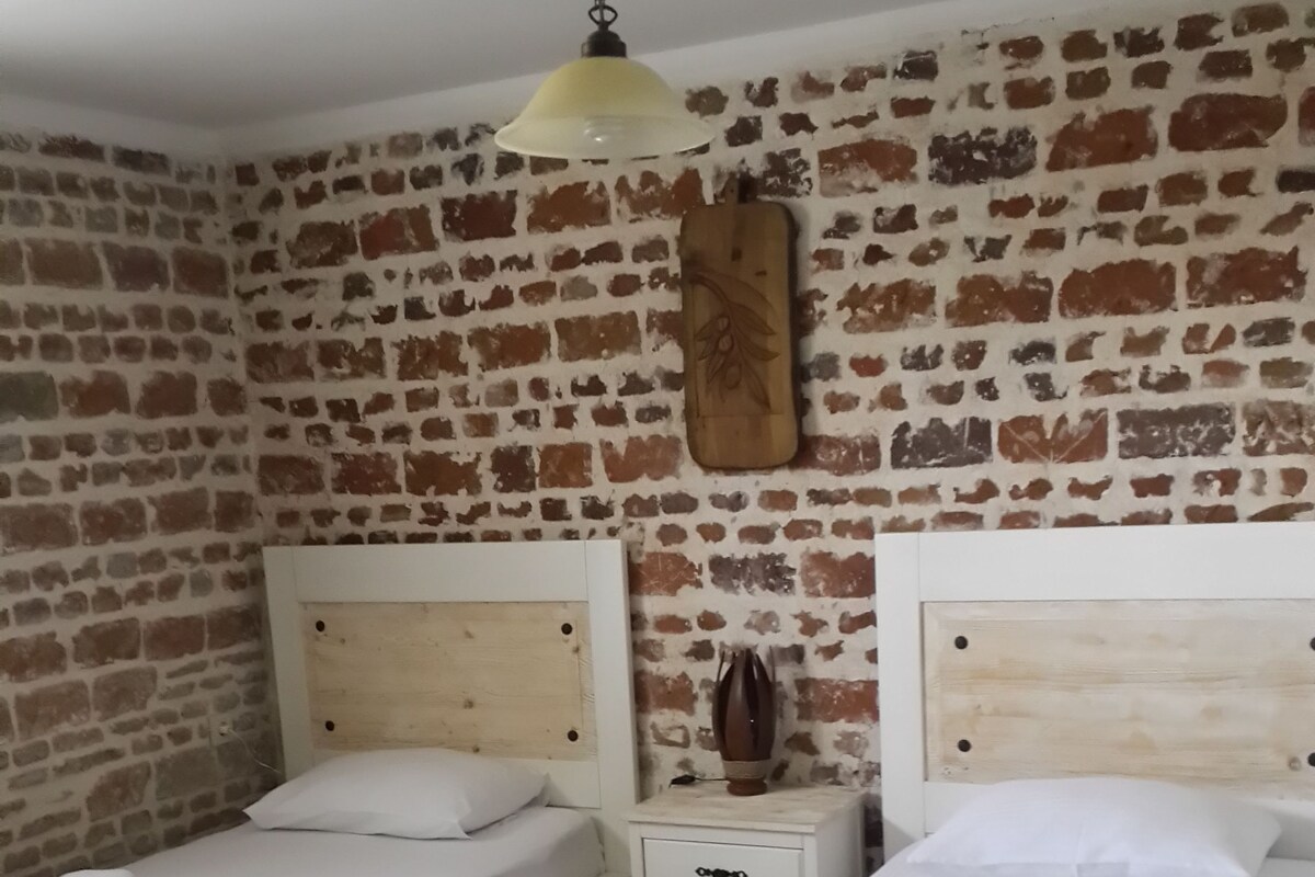 A room with two beds, a brick wall, a wooden headboard, a nightstand, and a hanging lamp.